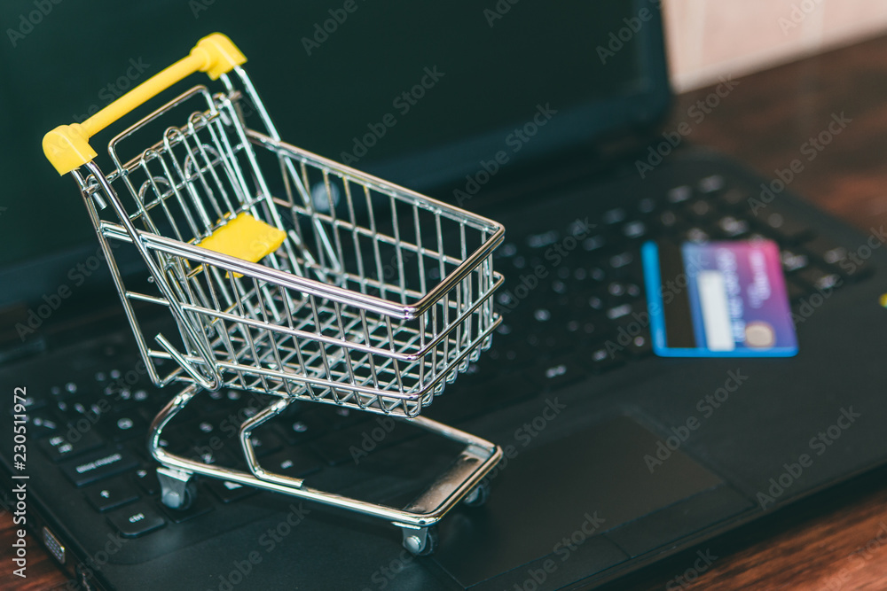Small trolley and a credit card on a black computer. Doing the shopping online to the supermarket concept. Earn money buying on Internet. Black Friday offers.