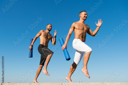 Forward to healthy lifestyle. Men with yoga mat captured in motion blue sky background. Sportsman with mat running. Run training outdoor. Runners hurry to stretch muscles after training. Yoga classes