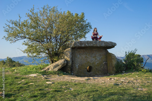 Girl sitting and meditating on ancient Dolmen and blue sky background