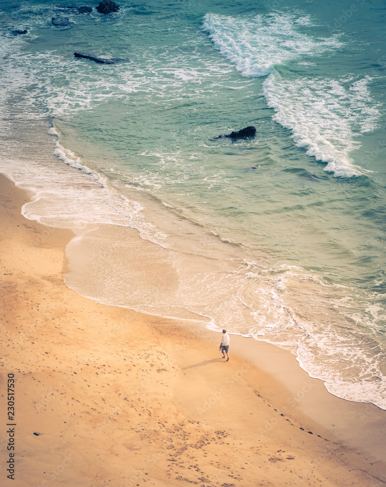 From above view of young man walking on beach along sea shore near water in Biarritz, France.
