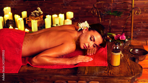 Massage of woman in spa salon. Girl on candles background in massage spa salon. Luxary interior in oriental therapy salon. dry flowers in wooden vases. Spot light on dark background.