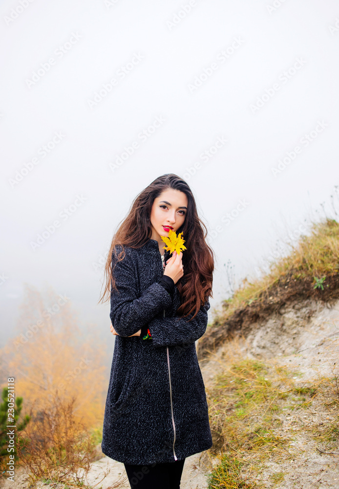 A beautiful lady dressed in a coat holds a yellow leaf in her hand A beautiful lady dressed in a coat holds a yellow leaf in her hand
