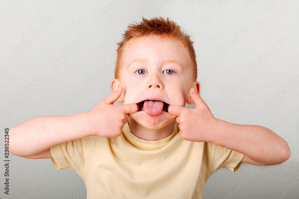 Fiery redhead young boy pulling a face, fingers in his mouth tongue ...