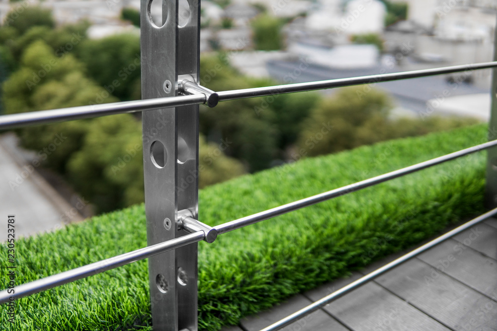 Details of fence made of stainless steel profile with an artificial raffa on the background. Details of fence made of stainless steel profile with an artificial raffa on the background.