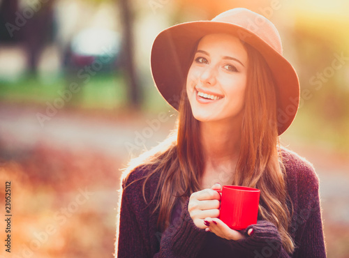 Beautiful redhead girl with cup in the park.