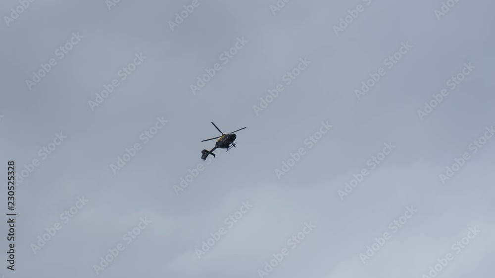 Helicopter marked Police is flying in overcast sky above in England, United Kingdom