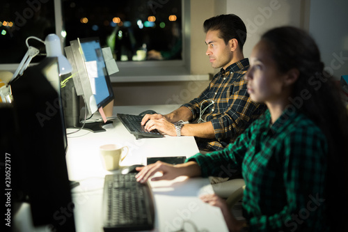 Side view portrait of two computer programmers working in dark office, focus on man typing at computer keyboard at night, copy space