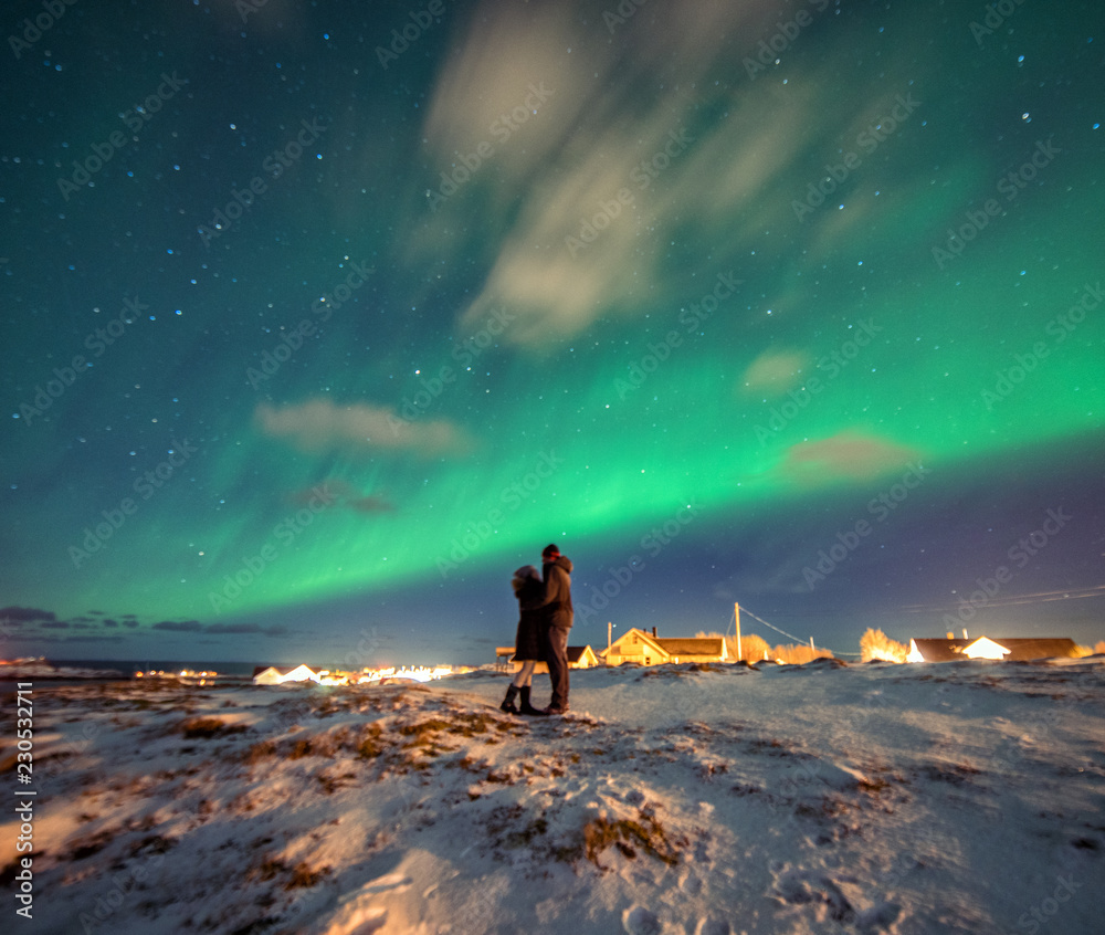 A couple admires the Northern Lights in the mountains of Reine, Norway. Lofoten Islands