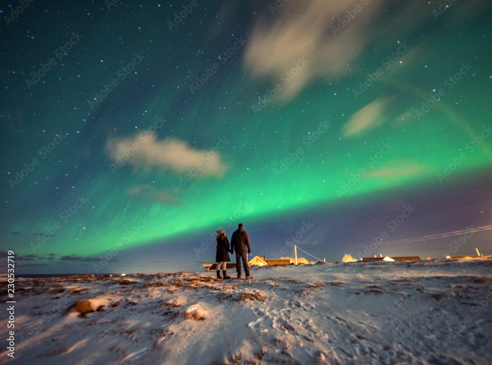 A couple admires the Northern Lights in the mountains of Reine, Norway. Lofoten Islands