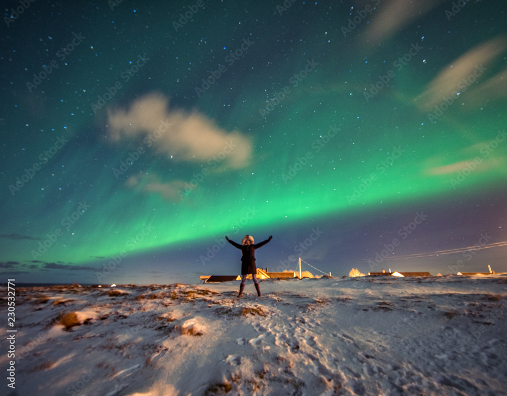 Woman tourist admires the Northern Lights in the mountains of Reine, Norway. Lofoten Islands