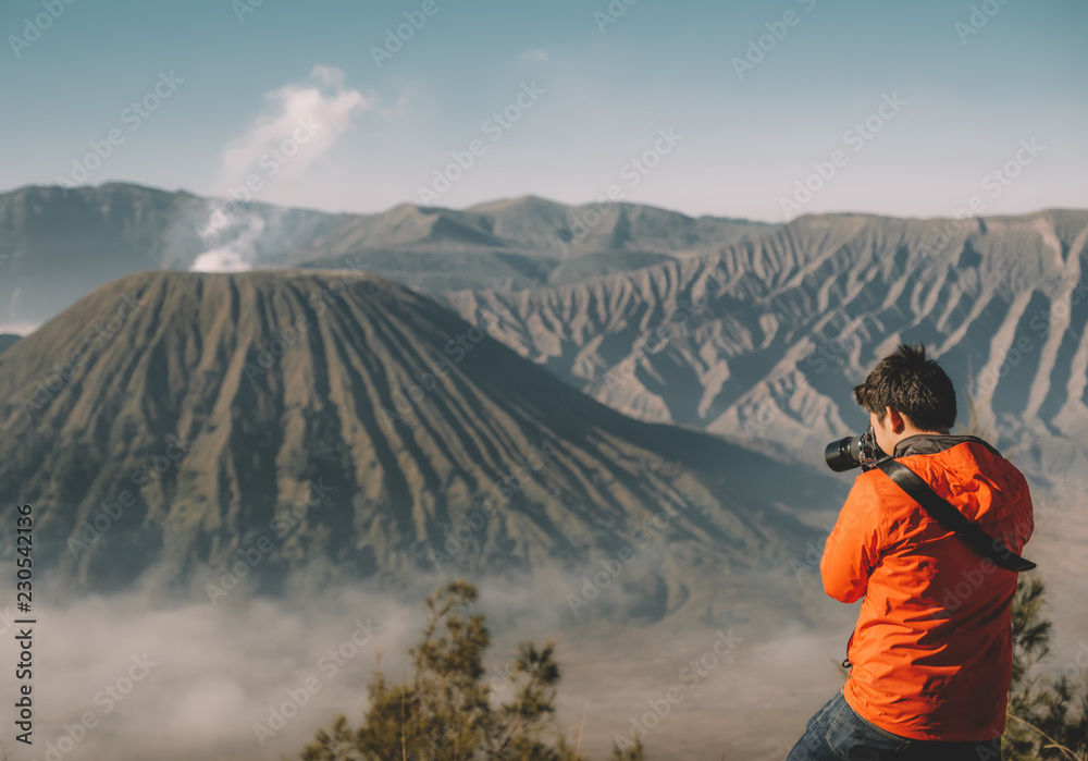 Young male adult photographer  shoot photo on a high mountain top in travel. Freedom concept. the active Bromo volcano, East Java, Indonesia