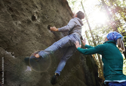 Принти на полотні A man rock climber climbing a rock and his partner insuring.