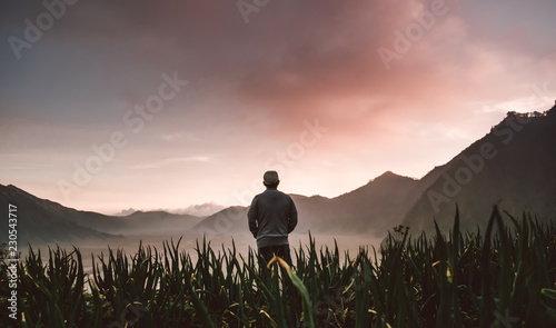 silhouetted man standing on the field in sunset with mountain background