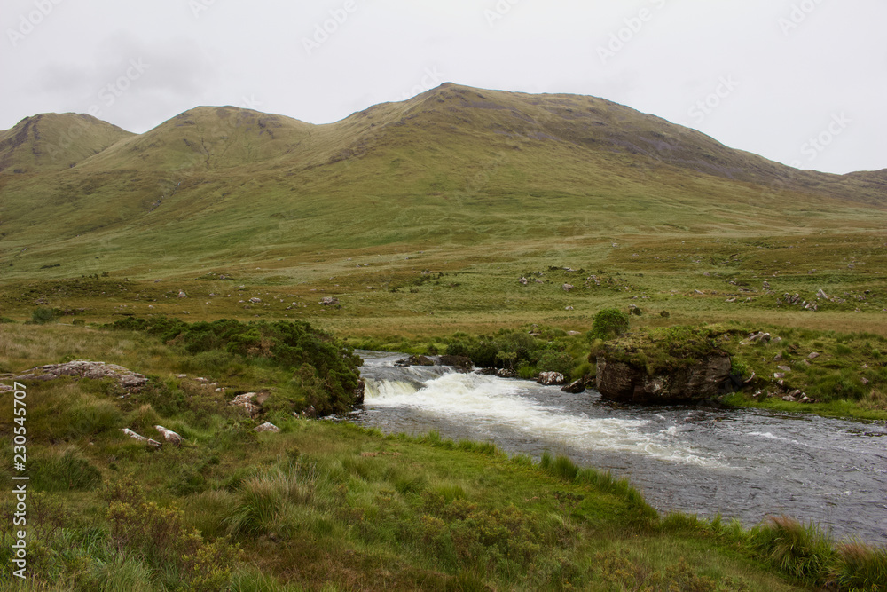 A small river flows through a remote area of the Connemara region of western Ireland, with mountains in the background A small river flows through a remote area of the Connemara region of western Ireland, with mountains in the background