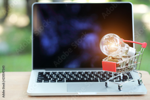 trolley and coins with electric glass bulb on computer, idea for shopping and online payment using as business background..