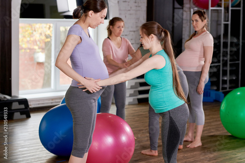 Side view portrait of two pregnant young women doing exercises together in prenatal yoga class