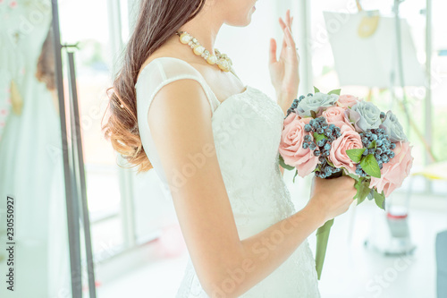 Side view of Bride holds a wedding bouquet and show her Wedding ring, white wedding dress, wedding details. photo