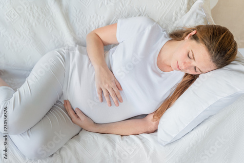 young pregnant woman in home resting on white sofa, no make up