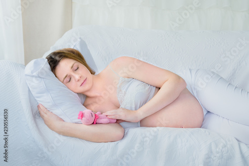 young pregnant woman sleeping on sofa with her handmade baby toy