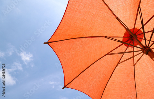 Closeup of a part of orange handmade cotton umbrella  with bright blue sky background. 