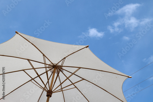 Closeup of a part of white handmade cotton umbrella  with bright blue sky background.