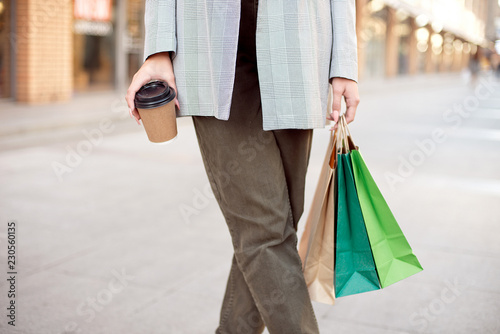 Close-up young fashion woman with shopping bags standing near storefront shop windows on the street outdoors.