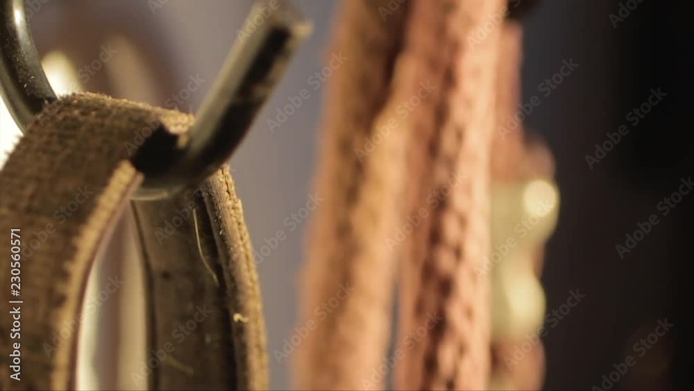 Dolly macro shot of riding gear like bridles and snaffles hanging in a stable.