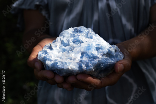 Close up of a woman holding a powerful healing blue calcite crystal in her hands in dark, moody light.	 photo
