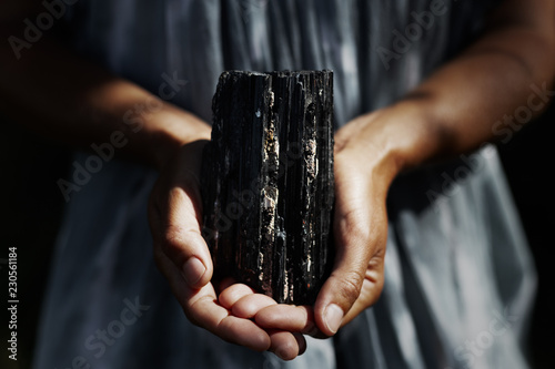 Woman's hands holding dark, powerful black tourmaline crystal in healing concept photo