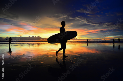 surfer carry a surf board on the beach with golden sunset background