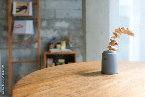 Dried plant in a gray ceramic vase on wooden table with warm cozy cafe interior background