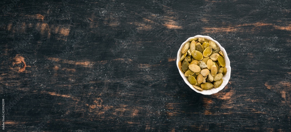 Naklejka premium Pumpkin seeds. On a black wooden background. Top view. Free copy space.
