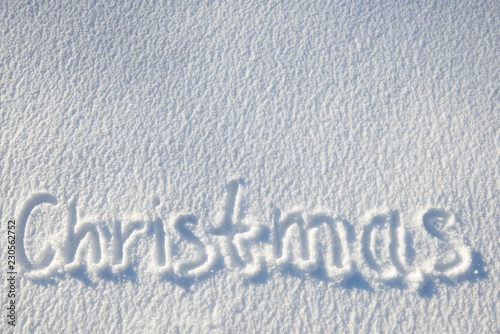 Christmas text written on snow for texture or background - winter holiday concept. Sunny day, bright light with shadows, flat lay, top view, clean and nobody