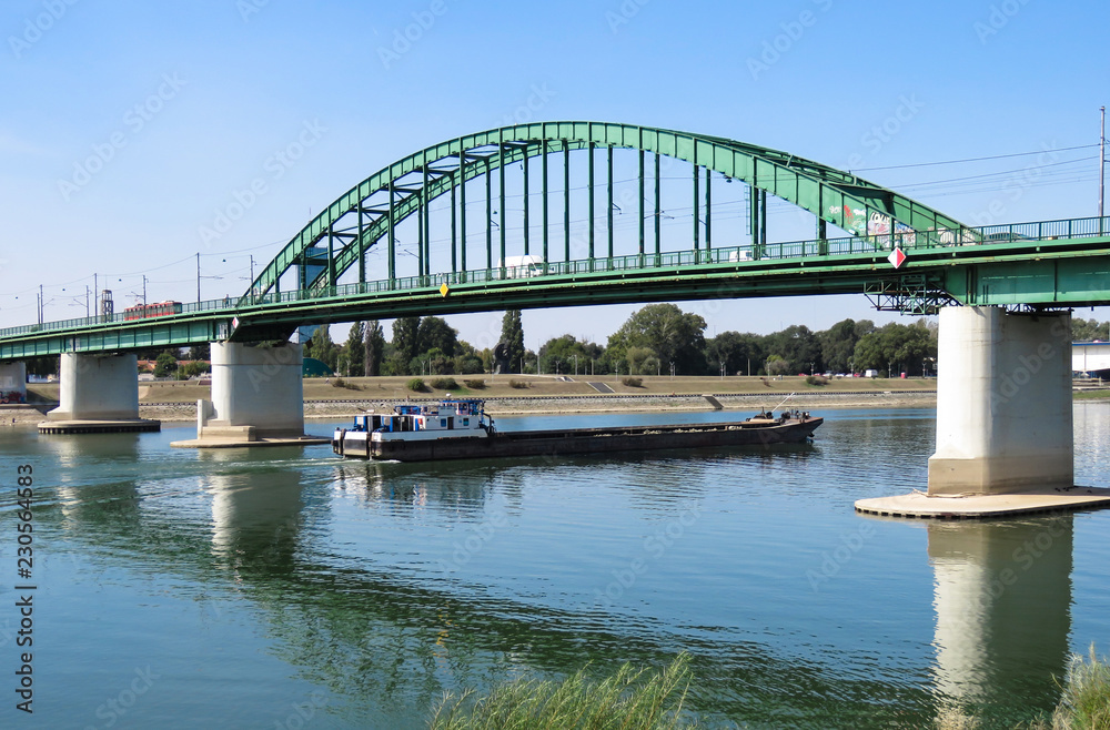Fototapeta premium Cargo ship passing under the old railway bridge on Sava river