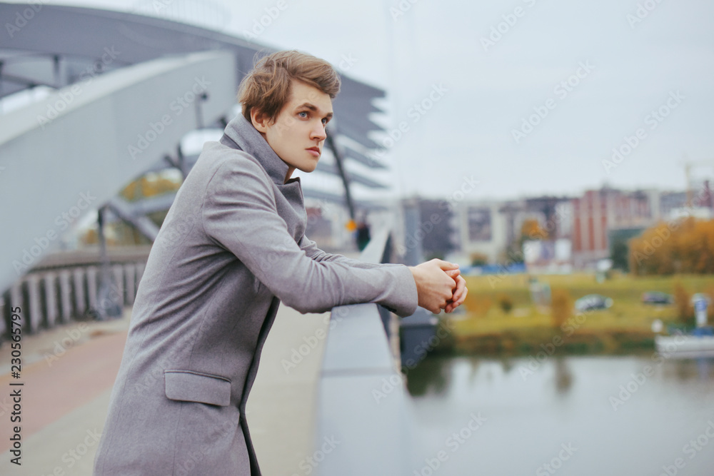 Young handsome man in coat. Fashionable well dressed boy smile in stylish coat. Boy outdoor at autumn. Elegant man with perfect hairstyle. Posing on the bridge. Fashion Young handsome man in coat. Fashionable well dressed boy smile in stylish coat. Boy outdoor at autumn. Elegant man with perfect hairstyle. Posing on the bridge. Fashion