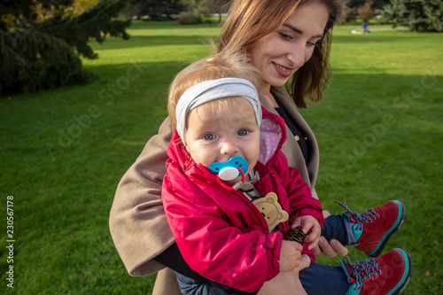 One year old girl sits by her mother in her arms and is happy looking at the camera.
