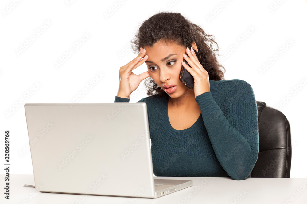 Beautiful dark skinned student talking on phone and working on her laptop on white background Beautiful dark skinned student talking on phone and working on her laptop on white background