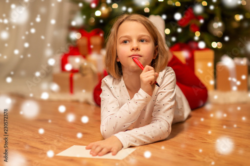 christmas, holidays and childhood concept - girl writing wish list or letter to santa at home photo