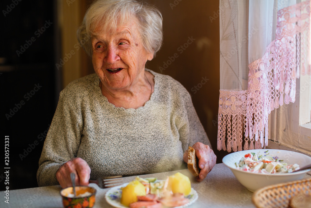 Elderly woman eat sitting at dinner table at home.