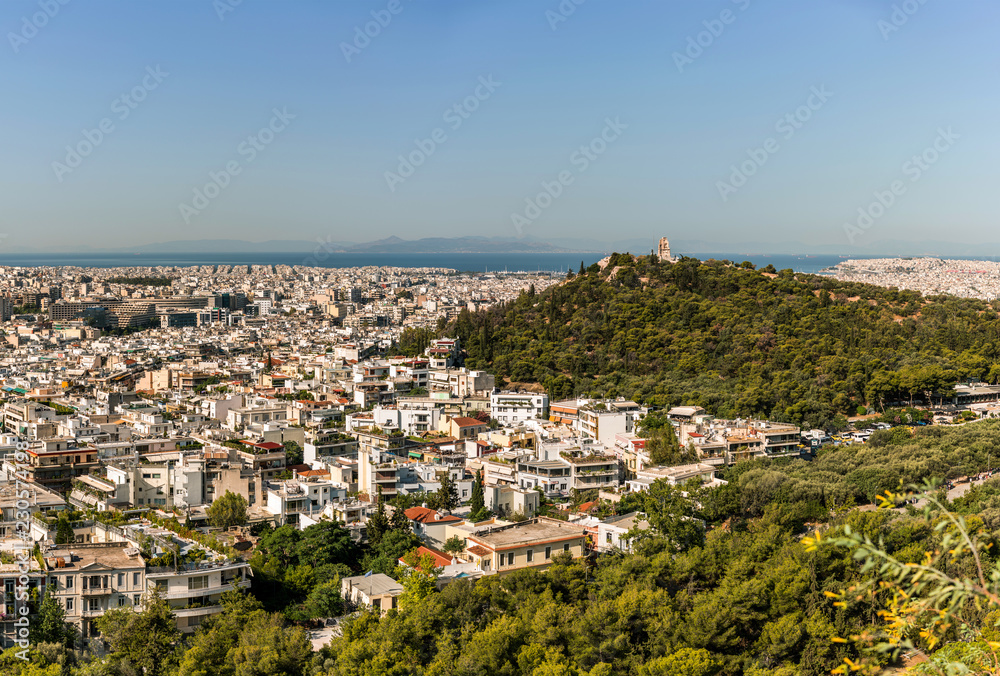 Athens city panorama with a green hill and aegean see on horizon.
