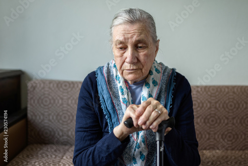 фотографія Sad old woman with a cane sitting on the couch