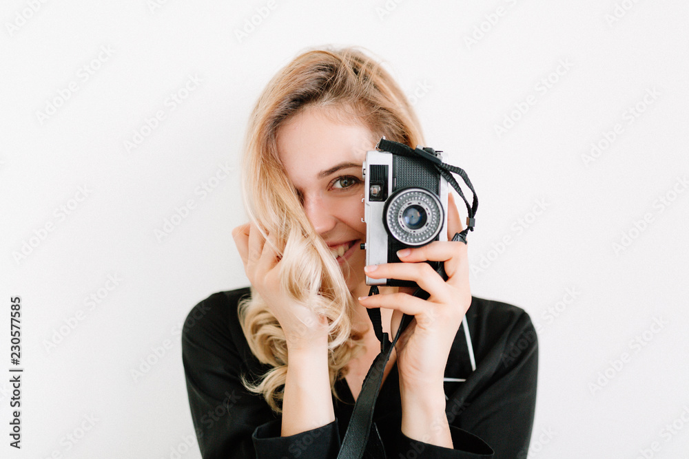 Close up portrait of happy smiling woman with blond hair and nude make up coveribg face with retro camera and posing to the camera in the sunlight Close up portrait of happy smiling woman with blond hair and nude make up coveribg face with retro camera and posing to the camera in the sunlight