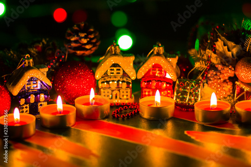 Merry Cristmas. Toy houses and candlelight. Christmas decorations on blurred background. Festive evening. Spruce branches and Christmas toys with bokeh. Copy space