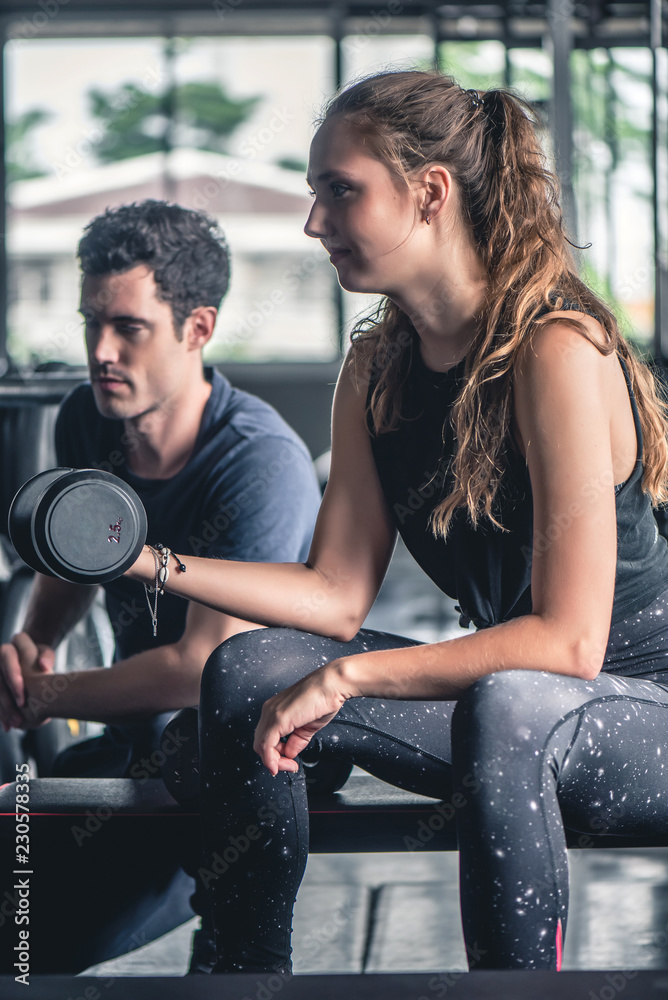 Cinematic tone of young attractive fitness woman exercise with dumbbell by trainer in gym. Cinematic tone of young attractive fitness woman exercise with dumbbell by trainer in gym.