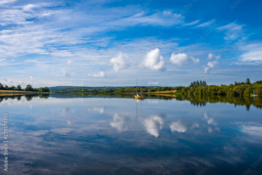 Scenic landscape reflection with yellow boat and white clouds in blue water. Arrow Lake, Sligo, Ireland