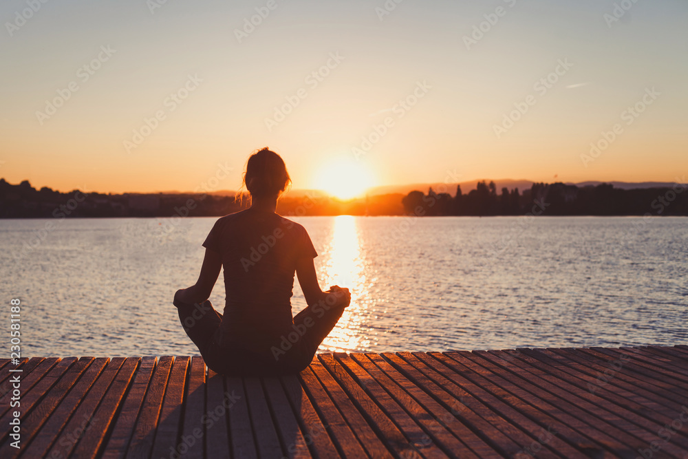 yoga, woman doing meditation and breathing exercises on wooden pier near lake, silhouette at sunset - obrazy, fototapety, plakaty 