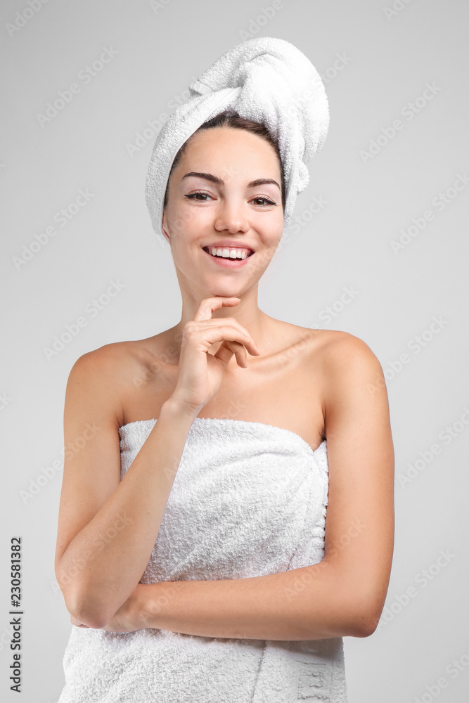 Beautiful young woman wrapped in towel on grey background