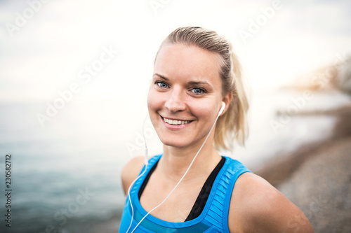 Young sporty woman runner with earphones standing on the beach outside.