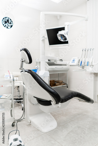 Vertical view of a dentist room with black seat. Modern dental practice. Dental chair and other accessories used by dentists