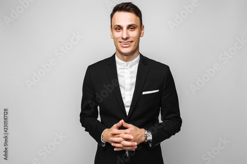 Portrait of a handsome young business man, male, in a classic black suit, on a gray background.